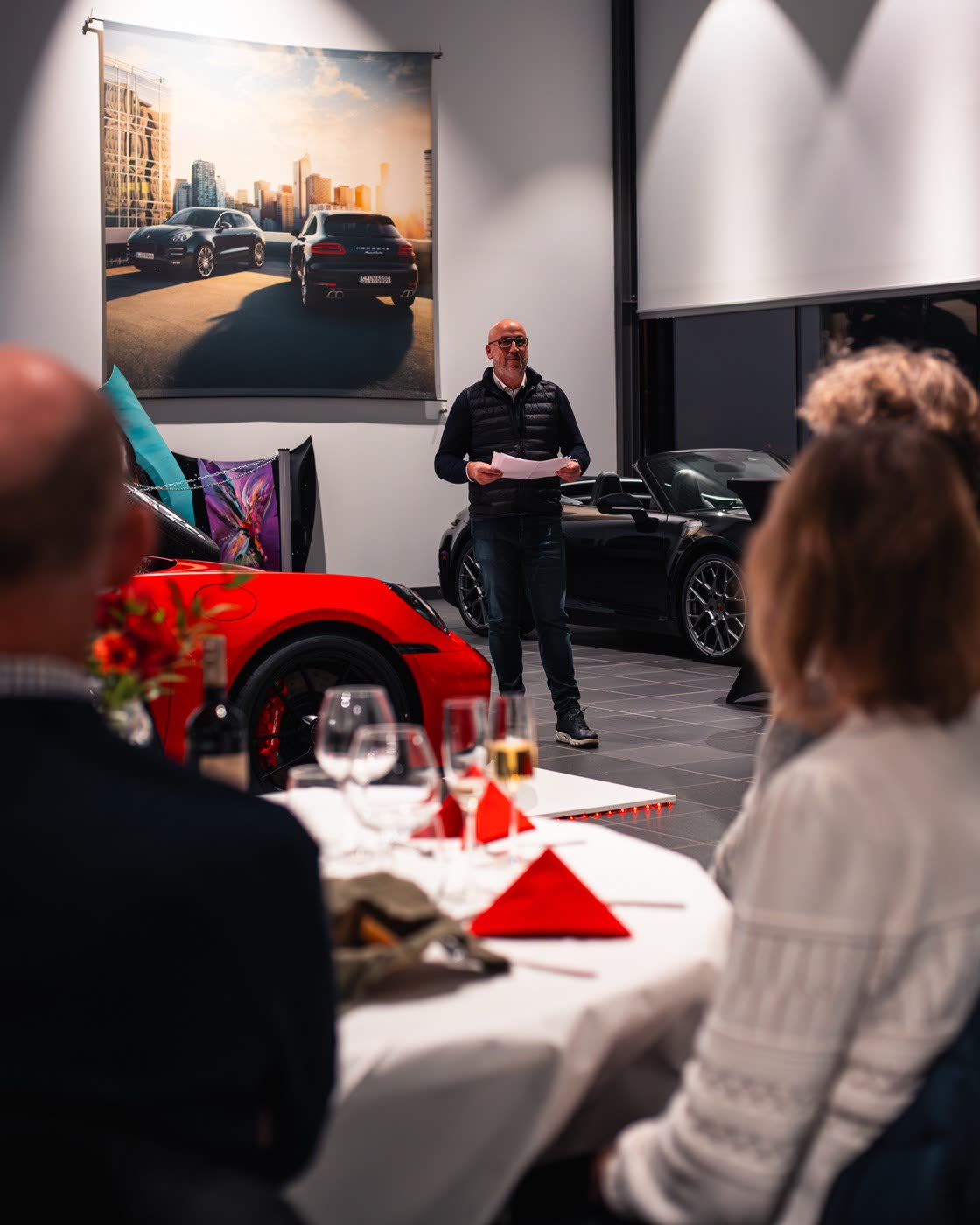 Speaker presenting at Porsche Center Kalmar Macan Electric reveal event with red 911 in foreground