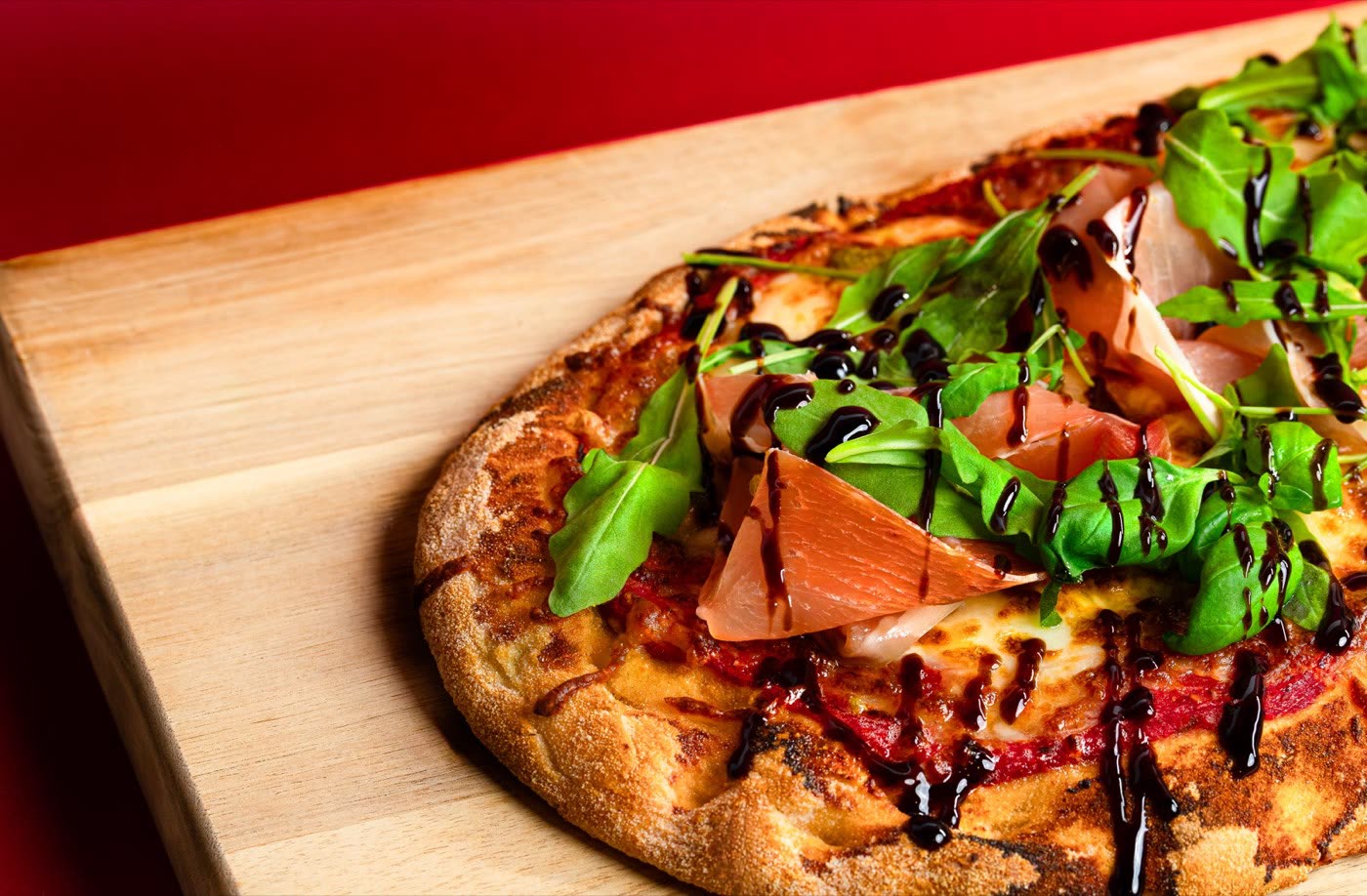 Prosciutto and rocket pizza with balsamic drizzle on a wooden board, Togo Kalmar
